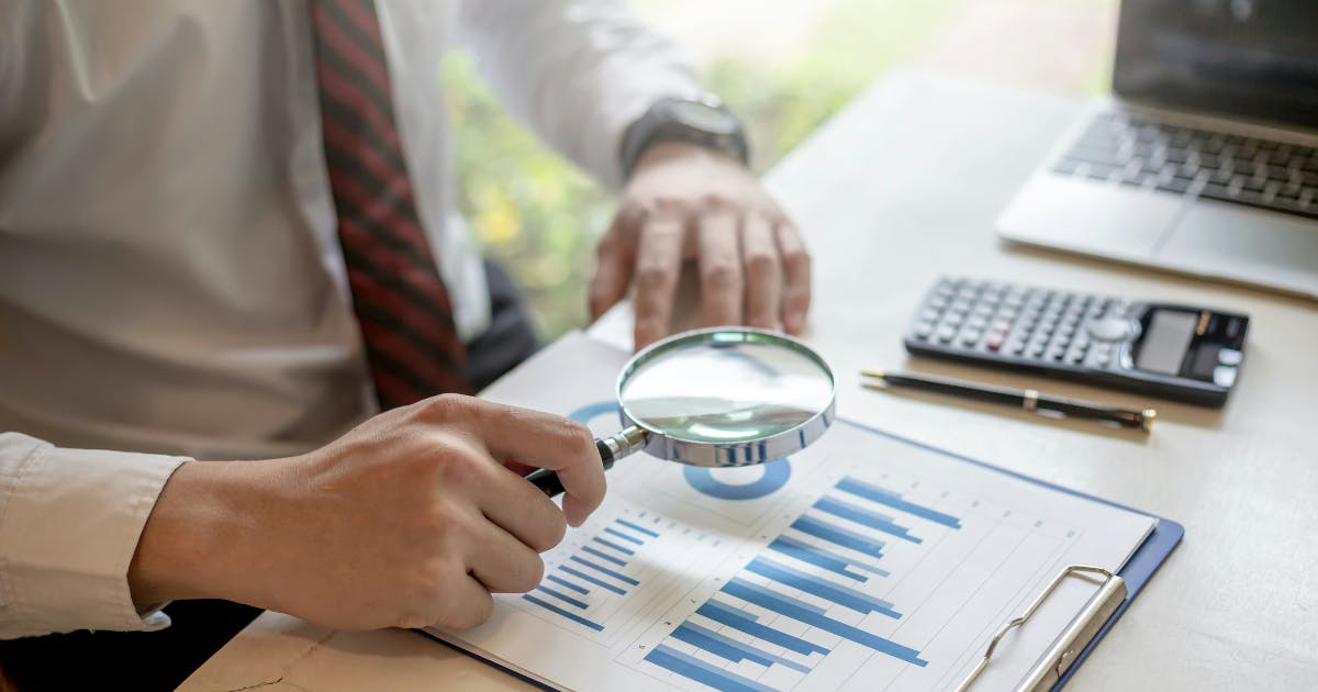 Close-up of a magnifying glass over a financial report, representing strategies for how to cut business travel and reduce travel costs in a business.